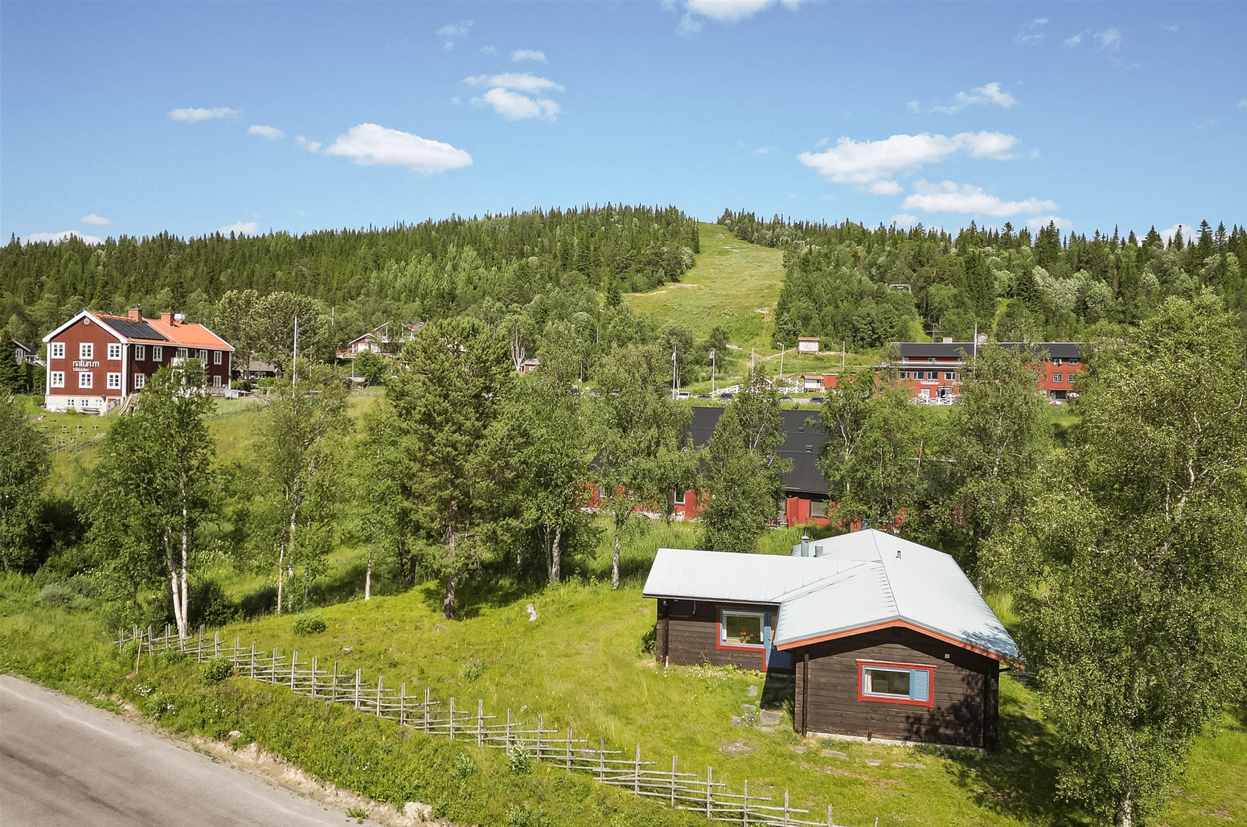 Stugan i Vålådalen i sommargrönska med fjällstationen i bakgrunden